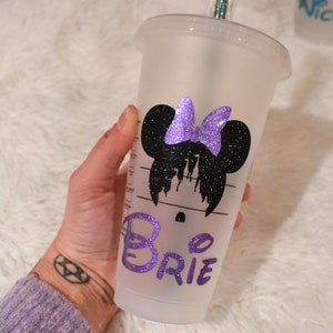 Puede incluir: Un vaso fr&iacute;o de pl&aacute;stico transparente con un dise&ntilde;o de Minnie Mouse con purpurina negra y un lazo de purpurina morada. El nombre "Brie" est&aacute; escrito en purpurina morada en el vaso. El vaso tiene una pajita verde.