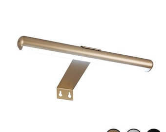 May include: A gold-toned metal picture light with a long, cylindrical horizontal bar and a flat, angled mounting bracket featuring two keyhole slots. The light source is integrated along the underside of the bar, emitting a bright white glow.