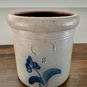 May include: A white ceramic mug with a black handle and the text "But First, Coffee" in a black, bold font. The mug is sitting on a white surface. The mug is approximately 4 inches tall.