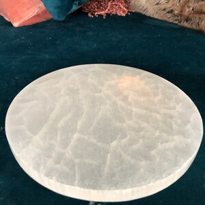 May include: A white, round selenite charging plate with a textured surface. The plate is on a dark blue background.