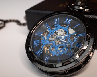 May include: A black pocket watch with a skeletonized blue and gold face. The watch has Roman numeral hour markers and a black chain.