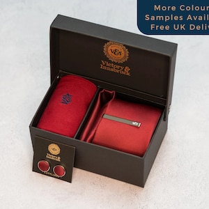 May include: A black gift box containing a red tie, pocket square, and cufflinks. The box is open and the items are visible. The box has the text "Victory & Innsbruck" on it.