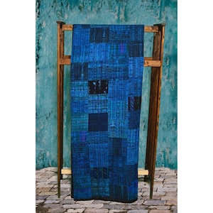 May include: A blue and black patchwork quilt is displayed on a wooden rack. The quilt is made of various shades of blue and black fabric, and the patchwork design is intricate and detailed.