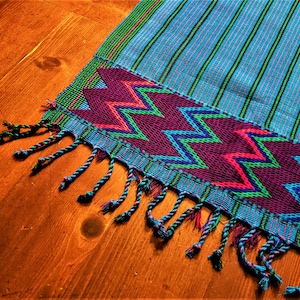 May include: A blue and purple woven throw blanket with a fringe border. The blanket has a geometric pattern of zigzags in green, pink, and blue.