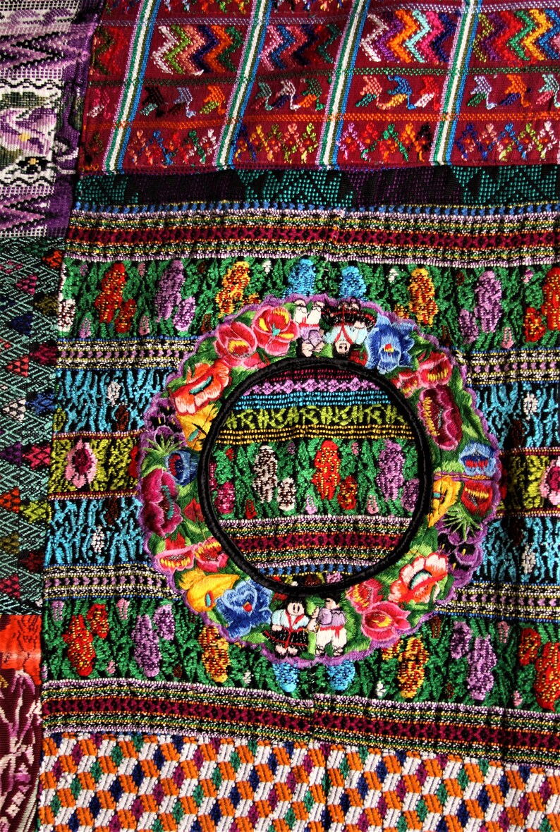 May include: A colorful textile with intricate embroidery featuring a circular design with flowers and figures. The textile is made up of various geometric patterns and vibrant colors, including red, green, blue, yellow, and purple.