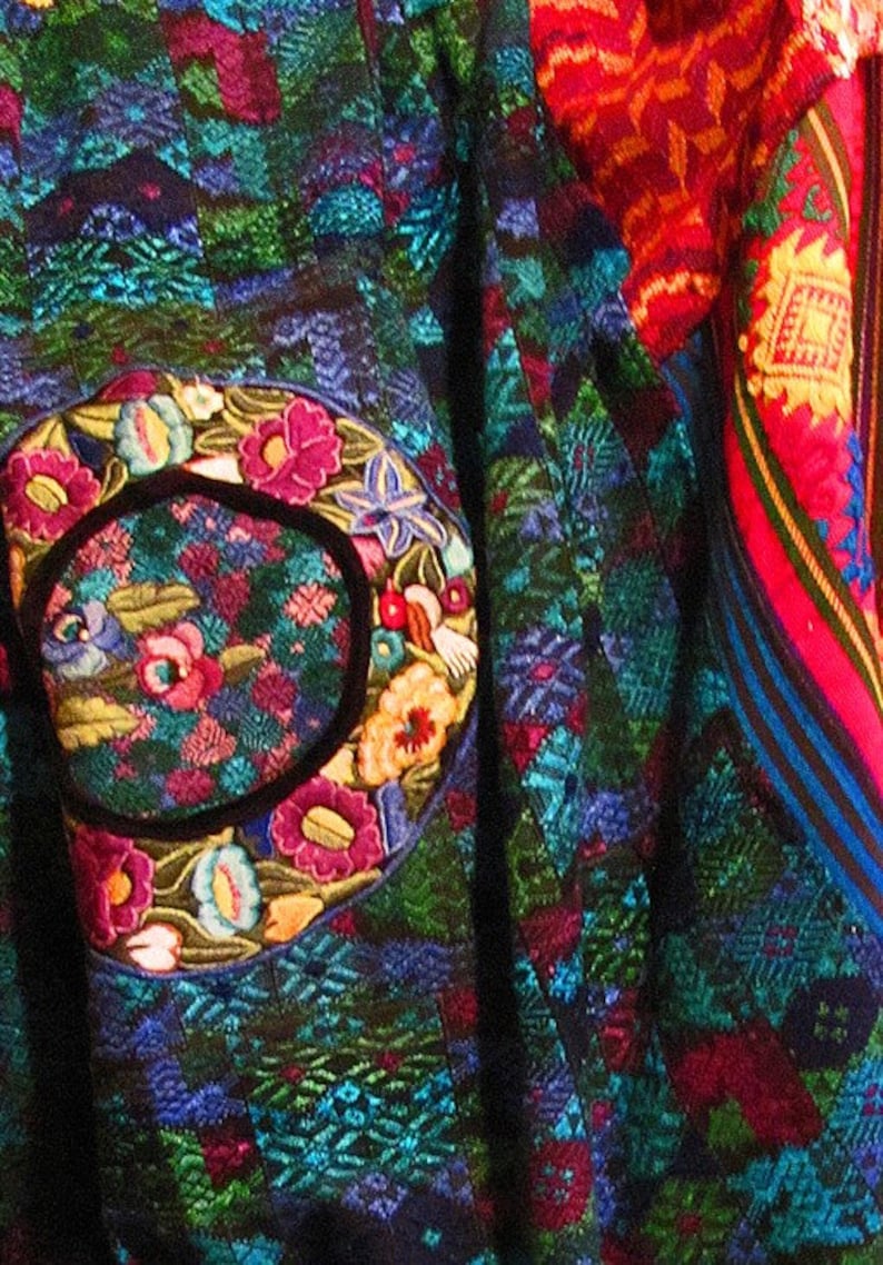 May include: A colorful textile with a large embroidered circle featuring flowers and leaves in shades of pink, blue, green, and yellow. The textile is woven with a geometric pattern in shades of blue, green, and red.