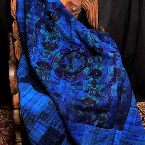 May include: A blue and black patterned fabric throw blanket draped over a wooden chair. The fabric has a floral design with a large circle in the center.