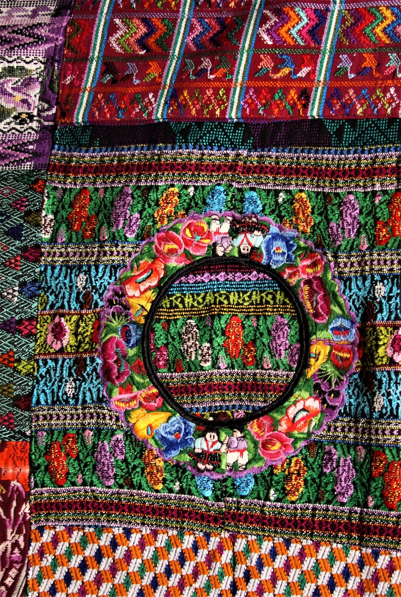May include: A colorful textile with intricate embroidery featuring a circular design with flowers and figures. The textile is made up of various geometric patterns and vibrant colors, including red, green, blue, yellow, and purple.