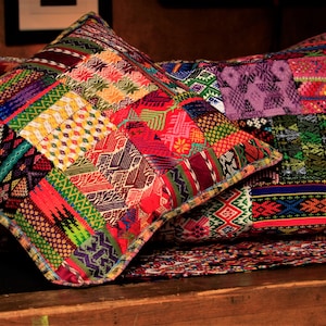 May include: Two colorful, hand-woven throw pillows with intricate patterns in shades of red, green, purple, and yellow. The pillows are made of a patchwork of different fabrics and have a fringed edge.