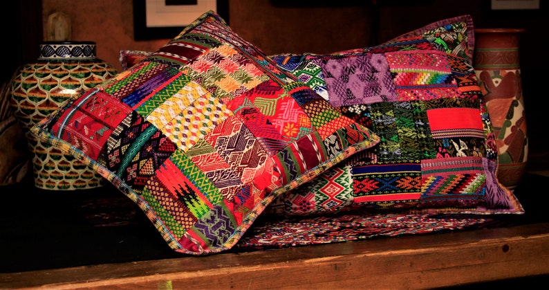 May include: Two colorful, hand-woven throw pillows with intricate patterns in shades of red, green, purple, and yellow. The pillows are made of a patchwork of different fabrics and have a fringed edge.