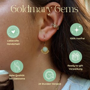 May include: A gold dangle earring featuring a round, pale green gemstone with a beaded edge, worn alongside a gold ear cuff. The image includes the text Goldmary Gems and icons with labels for handmade, rust-free, gift packaging, quality, and shipping.