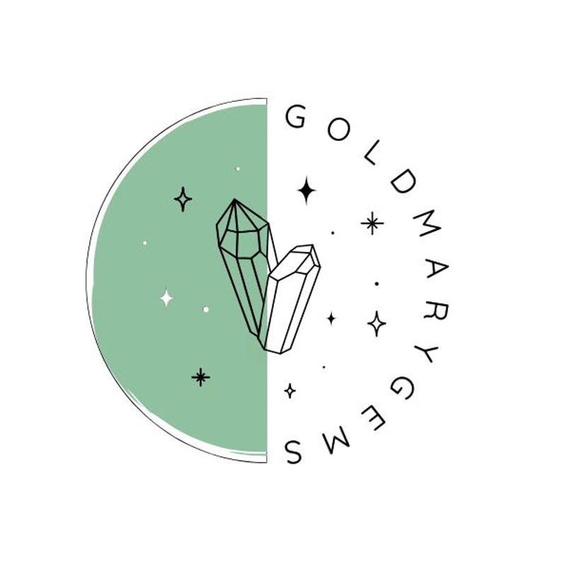 May include: A circular logo design split vertically between a solid sage green background and a white background. The center features black line art of two crystals surrounded by small star icons. The text GOLDMARY GEMS curves along the right side.