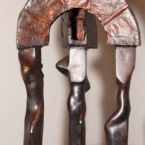 May include: A bronze sculpture depicting three figures standing beneath an archway. The figures are abstract and stylised, with smooth, rounded forms. The archway is crafted from textured bronze and has a rough, organic appearance.