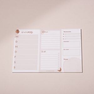 May include: A weekly planner with sections for "Wochensziele" (weekly goals), "Intention", "For mich" (for me), "To do", and "Focus". The planner has a light brown background with a brown watercolor design.