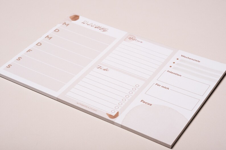 May include: A white weekly planner with a light brown watercolor design. The planner has sections for daily tasks, to-do list, weekly goals, intention, and focus.