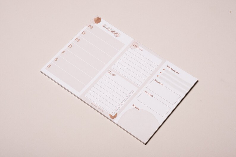 May include: A white weekly planner notepad with a pink and brown watercolor design. The notepad has sections for "To-do", "Focus", "For me", "Intentions", and "Wishes".