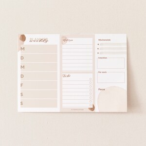 May include: A weekly planner with sections for notes, to-do list, weekly goals, intention, for me, and focus. The planner has a beige background with brown watercolor accents.