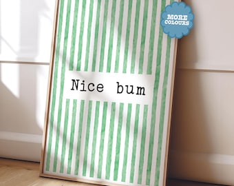 Puede incluir: Una impresión enmarcada con un marco de madera clara. La obra de arte presenta un fondo a rayas verdes y blancas con las palabras "Nice bum" en texto negro. Un gráfico azul en forma de nube en la esquina superior derecha dice "More Colours".