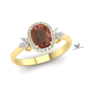 Puede incluir: Anillo de oro con una piedra preciosa ovalada de color marrón rojizo, rodeada de pequeñas piedras claras. El anillo tiene una banda delgada y está adornado con pequeños grupos de piedras claras en forma de hoja a cada lado.