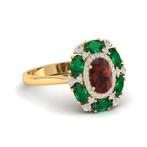 Peut inclure: Bague en or ornée d'une pierre rouge foncé ovale centrale, entourée d'émeraudes vertes et de petits diamants blancs. Le corps de la bague est en or poli, et le sertissage est complexe.