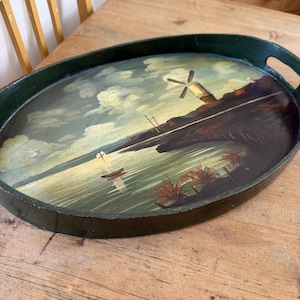 May include: Oval serving tray with a hand-painted landscape scene featuring a windmill, sailboat, and water. The tray has a dark green border and handles. The artwork includes shades of blue, green, brown, and white.
