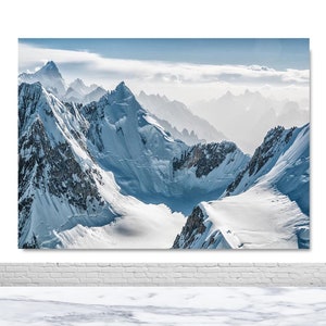May include: A panoramic view of snow-capped mountains with a blue sky and white clouds in the background.