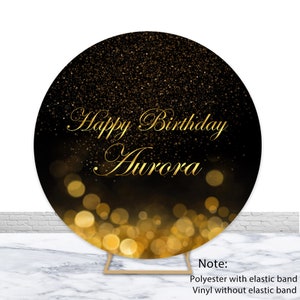 Puede incluir: Telón de fondo redondo negro con purpurina dorada y un texto dorado "Happy Birthday Aurora". El telón de fondo está decorado con luces bokeh doradas.