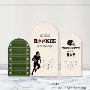 May include: Three arched display panels featuring football themes. One is green with white yard lines. Two are cream-colored with black text reading A Little Rookie is on the way and TOUCHDOWN it's a BOY, featuring football player and play diagrams.