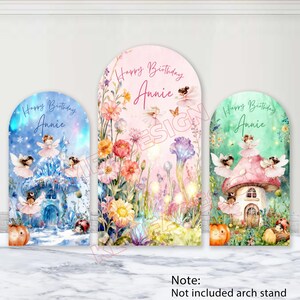 Peut inclure: Trois décors d'arche d'anniversaire avec des motifs de fées et de fleurs. Chaque décor porte l'inscription "Happy Birthday Annie". Les motifs comprennent une scène hivernale, un jardin fleuri et une maison champignon.