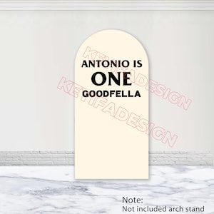 May include: A cream-colored arch-shaped sign with black text that reads "ANTONIO IS ONE GOODFELLA." The sign is displayed against a white wall and a marble-patterned surface. The words "KEIFADESIGN" are watermarked.