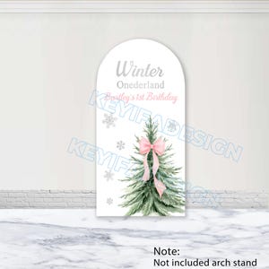 Puede incluir: Un letrero blanco en forma de arco con un diseño de árbol de Navidad en acuarela, adornado con un lazo rosa y copos de nieve. El texto dice "Winter Onederland, Bentley's 1st Birthday".