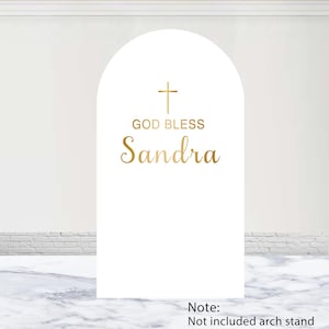 Pode incluir: Uma placa arqueada branca com um ícone de cruz dourada acima do texto "GOD BLESS" e o nome "Sandra" em uma fonte cursiva dourada. A placa é uma peça decorativa vertical plana, o suporte em arco não está incluído.