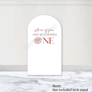May include: A white arched backdrop cover featuring red text that reads slice of fun AMY IS TURNING ONE, with a red line drawing of a pizza slice replacing the letter O in the word ONE. The design is printed on a smooth, vertical surface.