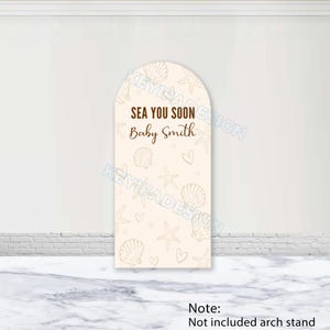 May include: A beige arch-shaped sign with a seashell and starfish pattern. The sign reads "SEA YOU SOON Baby Smith" in brown text. The bottom of the sign has a note that says "Not included arch stand".