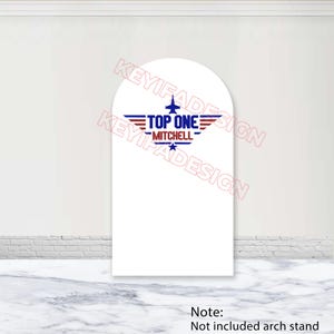 May include: White arch-shaped sign with a Top Gun-themed design. The design features a stylized jet, wings, and the text "TOP ONE MITCHELL" in red, white, and blue. A star is below the text. The sign is on a marble-patterned surface.