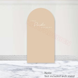 Könnte beinhalten: Eine beige gewölbte Hintergrundplatte mit dem weißen Text A LITTLE Pumpkin IS ON THE WAY. Das Design hat eine glatte, einfarbige Oberfläche mit einer abgerundeten Oberkante und wird als eigenständiges dekoratives Display für Veranstaltungen präsentiert.