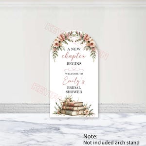 May include: An arched sign featuring a floral arrangement of pink roses and greenery at the top and a stack of vintage books at the bottom. The text reads A NEW chapter BEGINS WELCOME TO Emily's BRIDAL SHOWER in black and pink script fonts.