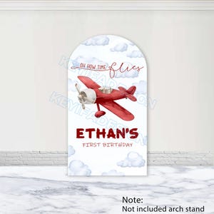 Op de afbeelding: Een rode vliegtuigafbeelding op een wit boogvormig bord met de tekst "Oh how time flies" en "Ethan's First Birthday". Het ontwerp bevat witte wolken en is geschikt voor een verjaardagsfeest.