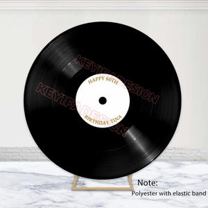May include: A black vinyl record-shaped backdrop with gold text that reads "Happy 60th Birthday Tina." The backdrop is supported by a wooden stand. The backdrop is made of polyester with an elastic band.