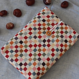 May include: A rectangular, woven fabric case with a button closure. The case features a colorful checkered pattern in shades of red, orange, green, and beige. Several brown chestnuts are scattered around the case on a light blue surface.