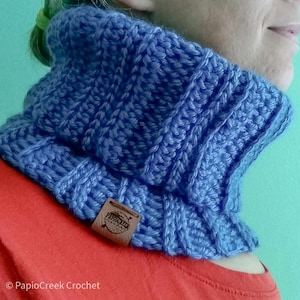 May include: A blue crocheted cowl neck warmer with a brown leather tag that says "PapioCreek".