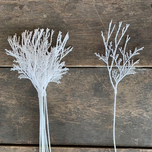 May include: Two bunches of white artificial branches with a feathery texture. The branches are on a wooden background.