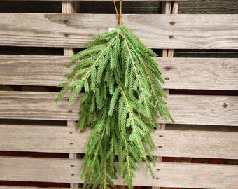 May include: A green fir branch bundle with a brown twine loop for hanging. The bundle is composed of multiple green needles and is displayed against a rustic wooden pallet background. The natural tones create a simple, yet elegant aesthetic.