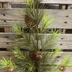 May include: A green pine sprig with brown pine cones. The sprig is against a wood background.