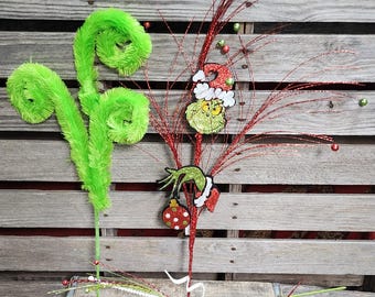May include: Three Christmas-themed artificial floral stems. One stem features a green, fuzzy, curly design. Another stem has red glitter sprigs with a green and red Grinch character ornament. The third stem has red glitter sprigs with white beads.