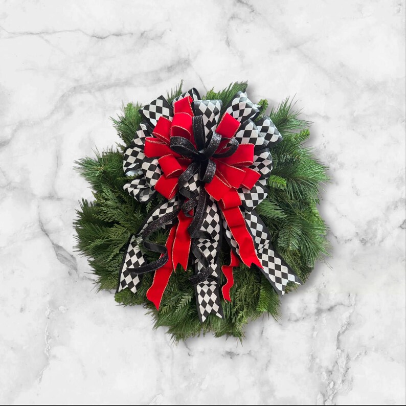 Puede incluir: Una corona decorativa con una base de agujas de pino verdes. La corona est&aacute; adornada con un gran lazo con cinta de terciopelo roja, cinta a cuadros en blanco y negro y cinta con purpurina negra. Un acento decorativo para el hogar.