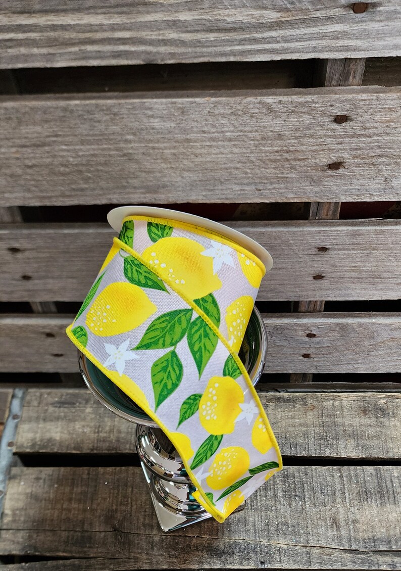 May include: A roll of yellow and white ribbon with a lemon print. The ribbon is on a wooden surface.