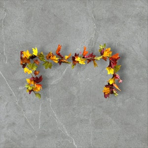 May include: A garland of fall leaves in shades of red, yellow, and orange, arranged in a curved shape against a gray marble background.