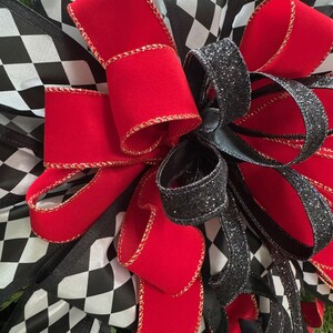 Puede incluir: Primer plano de un lazo decorativo con cinta de terciopelo roja con ribete dorado, cinta negra con purpurina y cinta a cuadros blancos y negros. El lazo es probablemente para una corona u otra decoraci&oacute;n navide&ntilde;a.