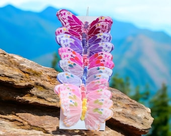 May include: A vertical display card featuring a column of six decorative butterfly ornaments in a gradient of colors, ranging from deep magenta and purple at the top to light pink and yellow at the bottom, with translucent wings.